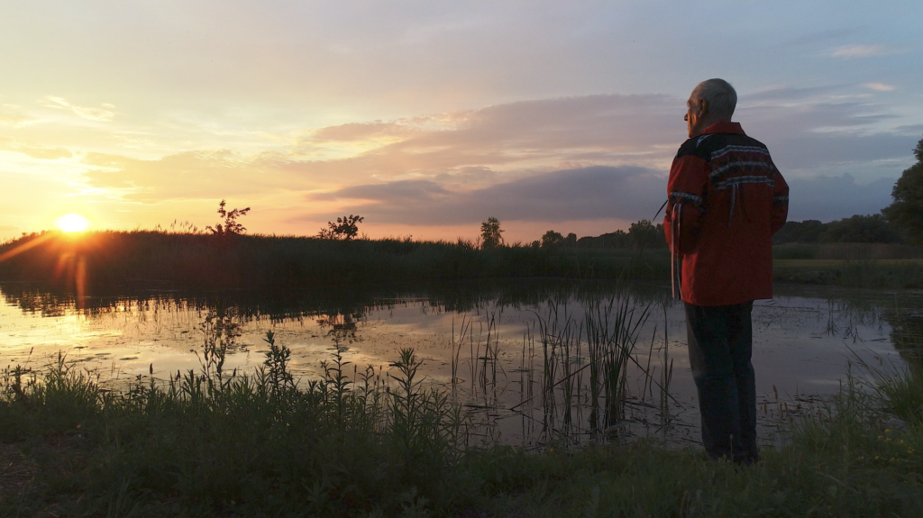 A man standing next a lake watching the sunset