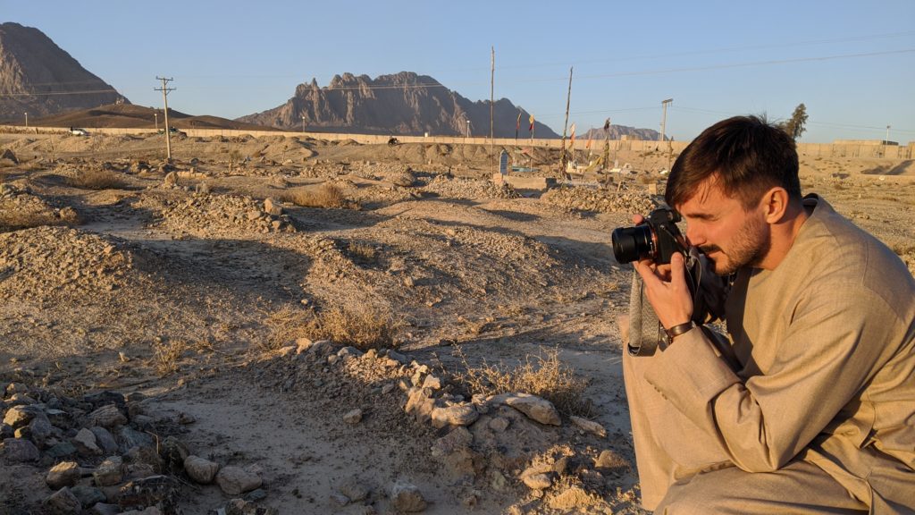 Journalist Graeme Smith crouches while photographing arid Afghanistan landscape