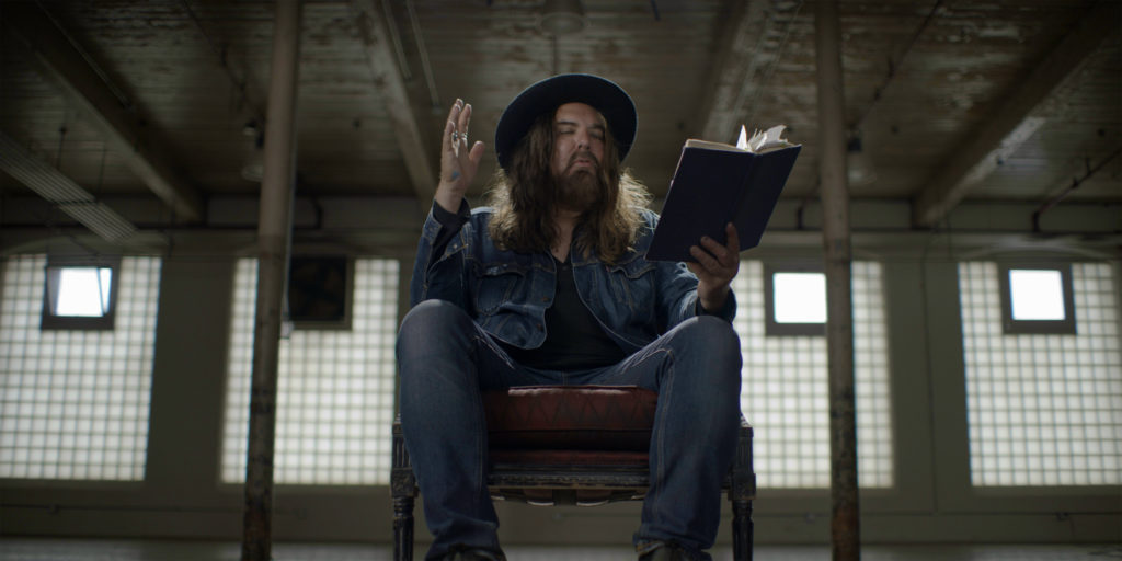 Tom Wilson sitting in a chair in a warehouse reading