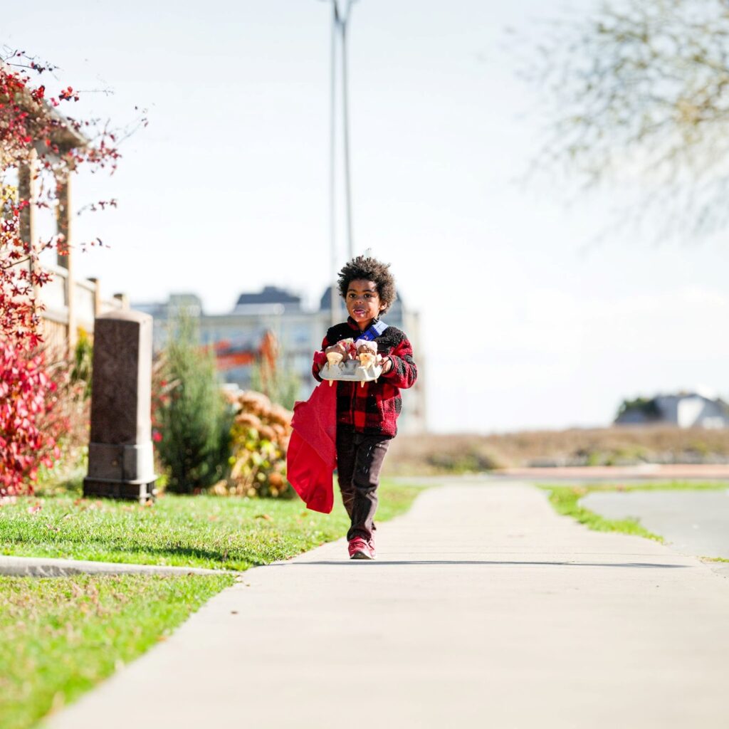 A young kid carrying a tray of ice cream down the sidewalk by himself.