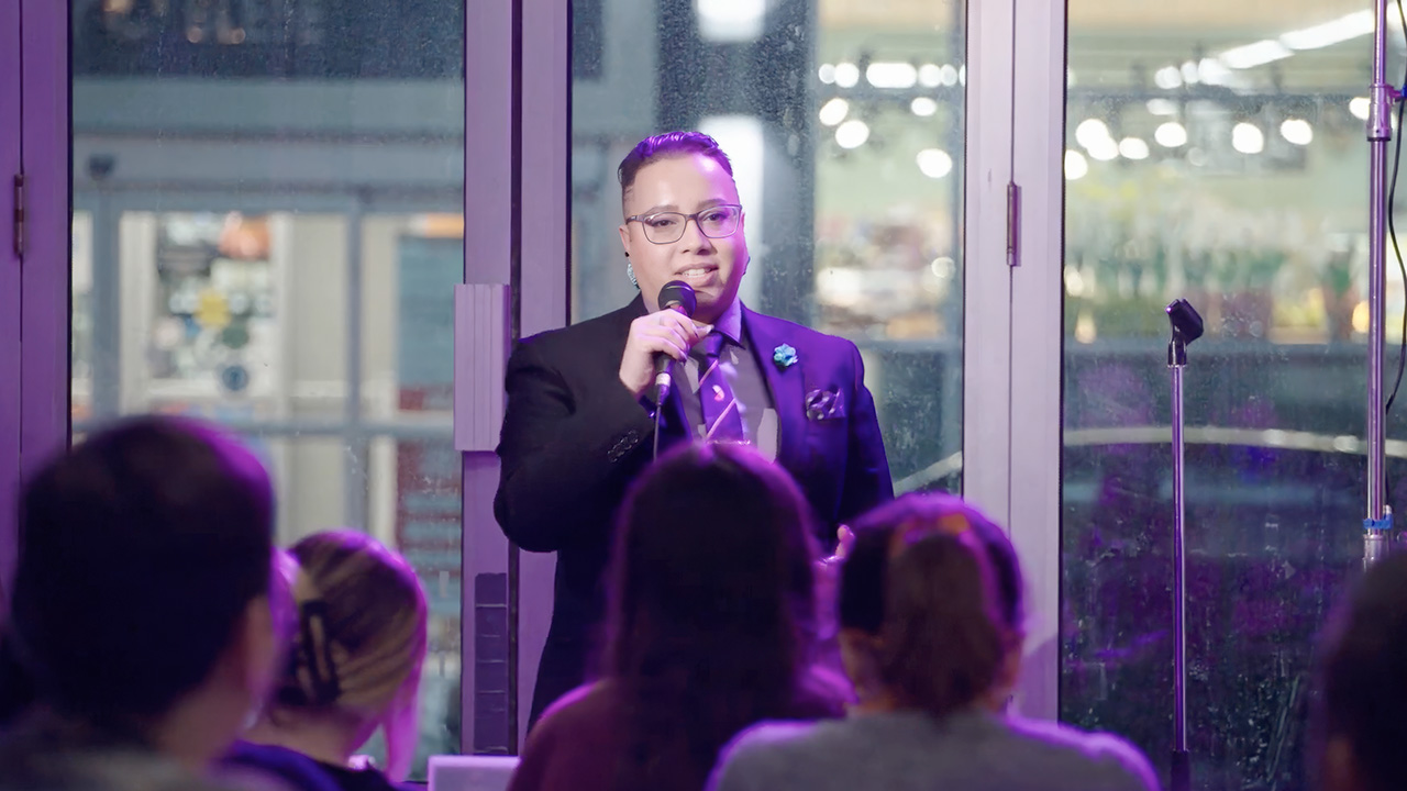 Janelle Niles speaking into a microphone in front of an audience indoors.