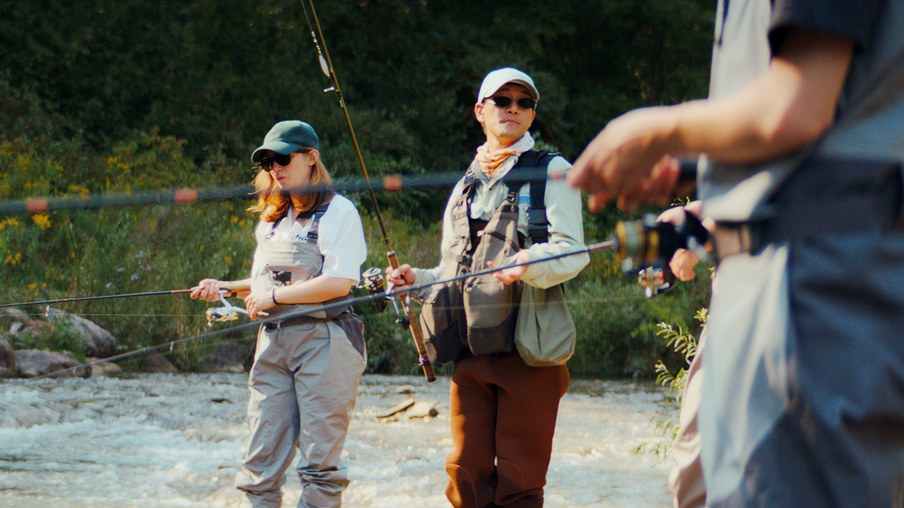 People fly fishing in a shallow river outdoors.