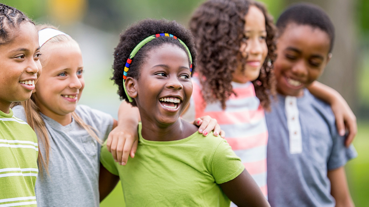 Group of children standing close together outdoors with their arms around each other.