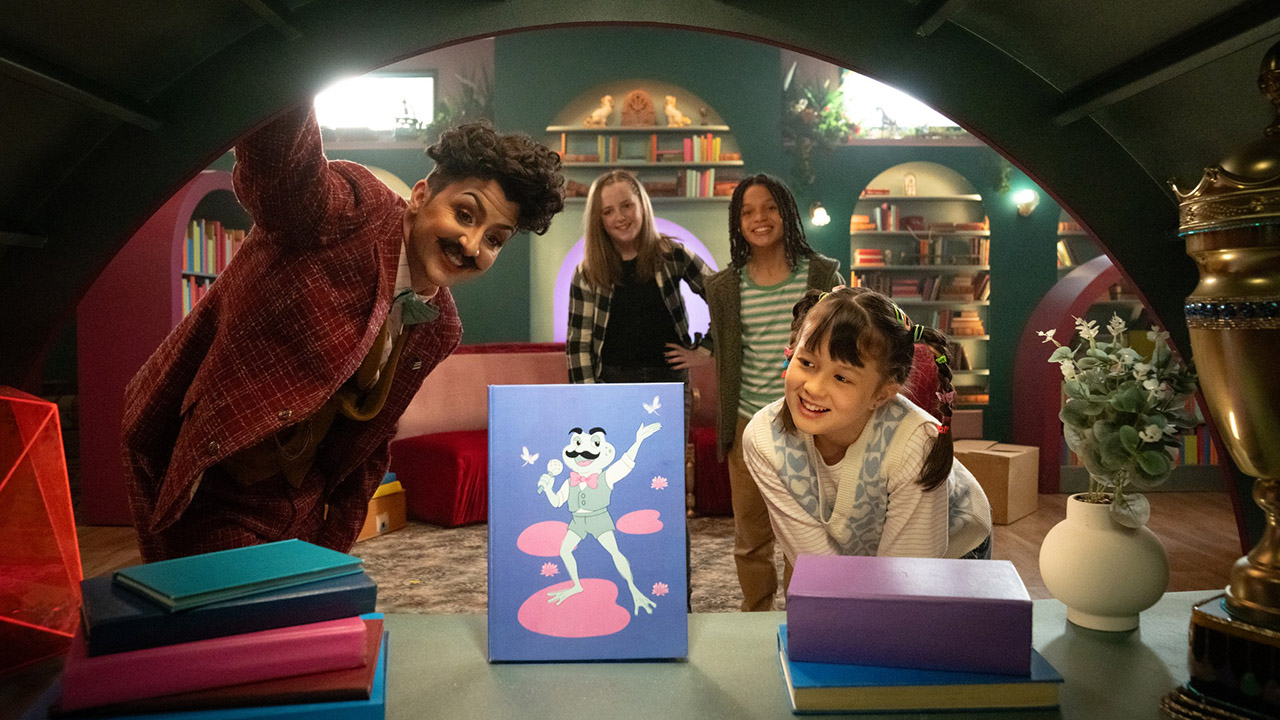 Mr. Hugo and friends gathered around a table viewing a colorful illustrated poster in a cozy room.